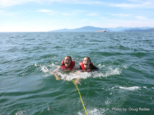 Ella Parker and SLLP facilitator, Megan Rempel being towed behind the Voyageur canoe in English Bay at the end of the SLLP journey.