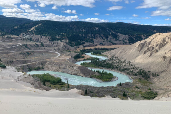 A glacial blue river winds through sandy hills.